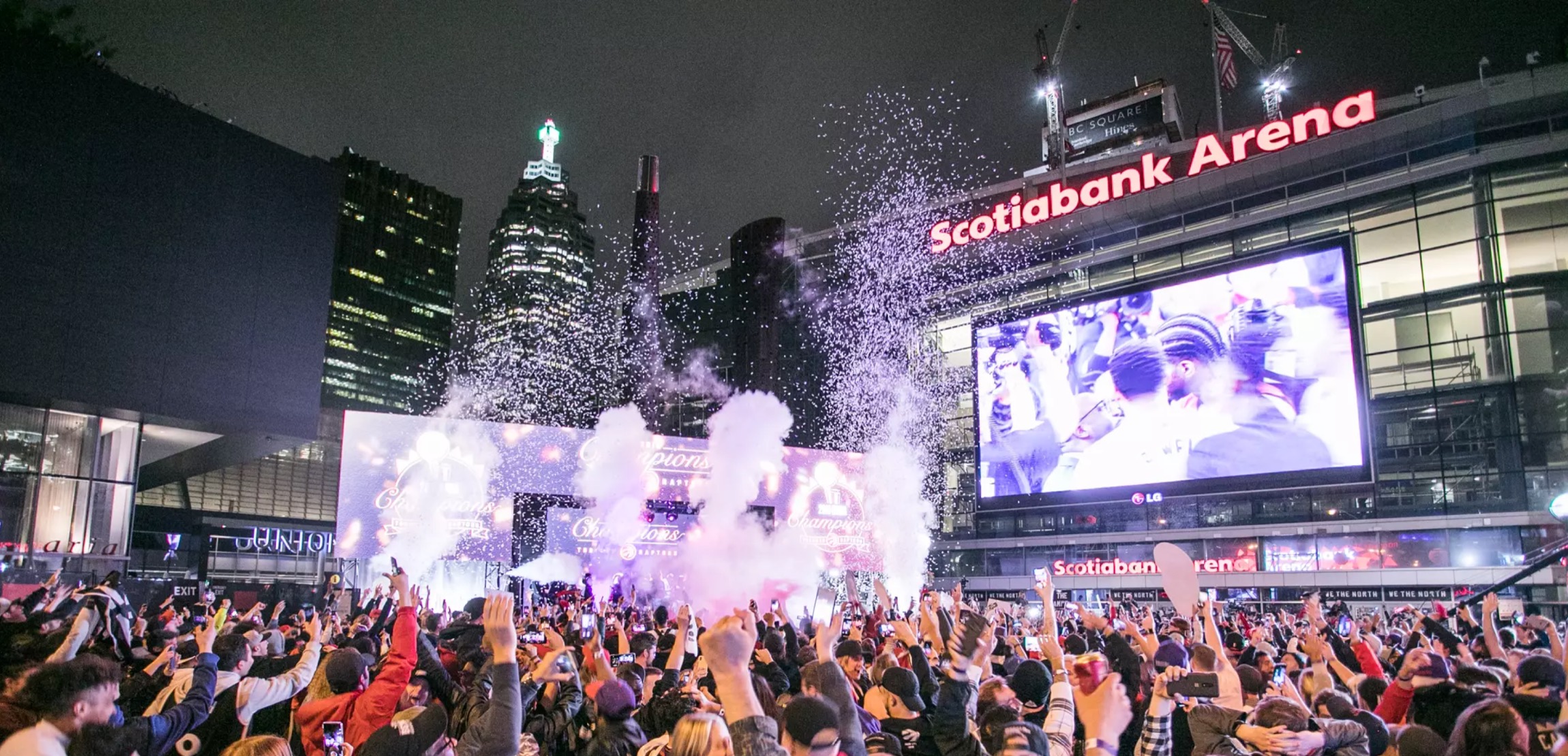 A crowd outside Scotiabank Arena at night, phones raised, confetti in the air during a championship celebration